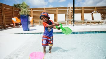 A child playing in a pool with a green shovel and a pink bucket.