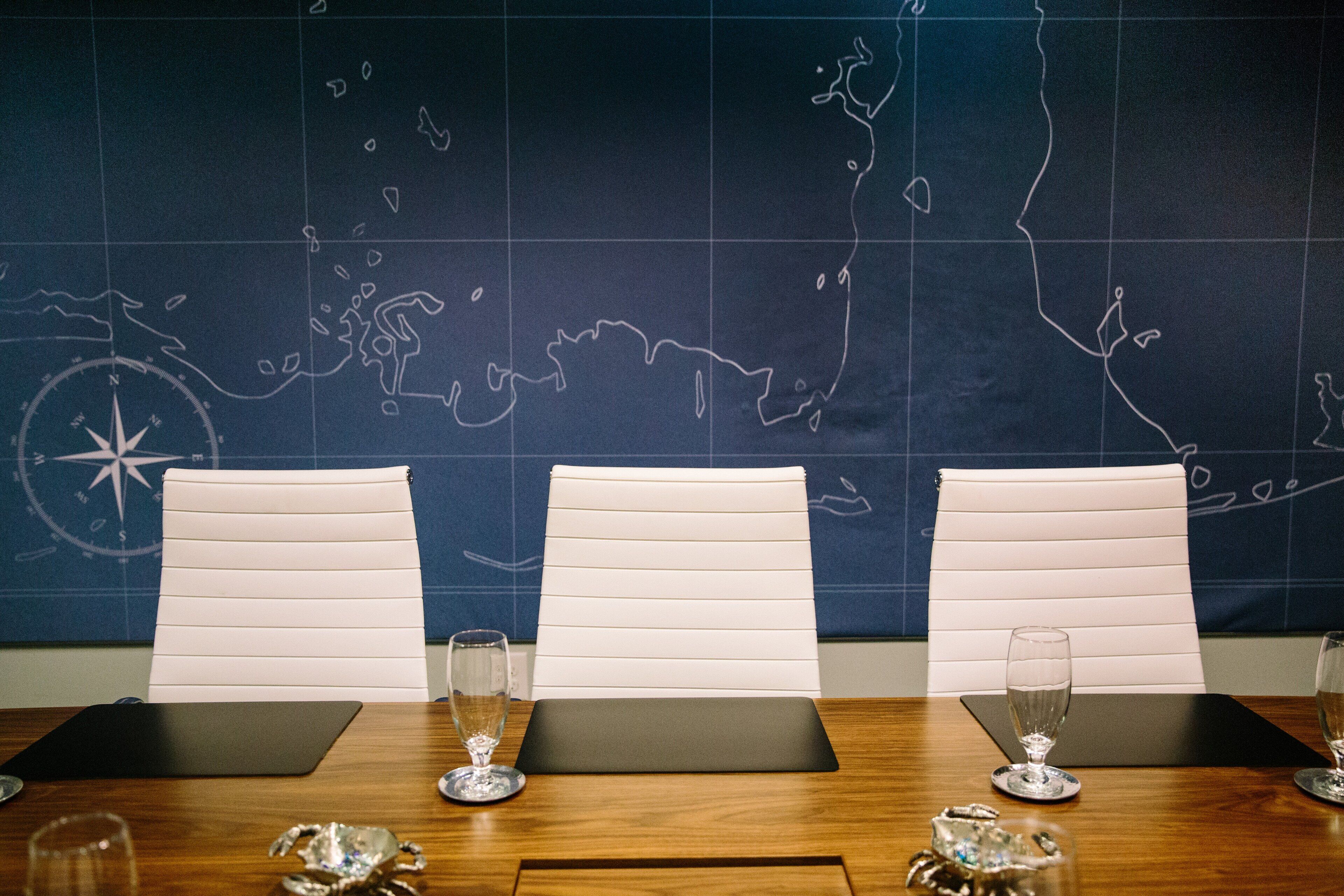 Une salle de conférence avec trois chaises blanches, une table en bois et une carte du monde accrochée au mur.