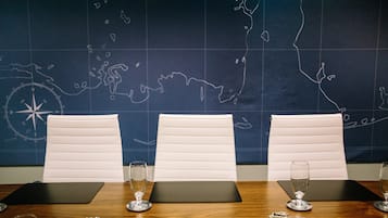 Un salón de conferencias con tres sillas blancas, una mesa de madera y un mapa mundial en la pared.