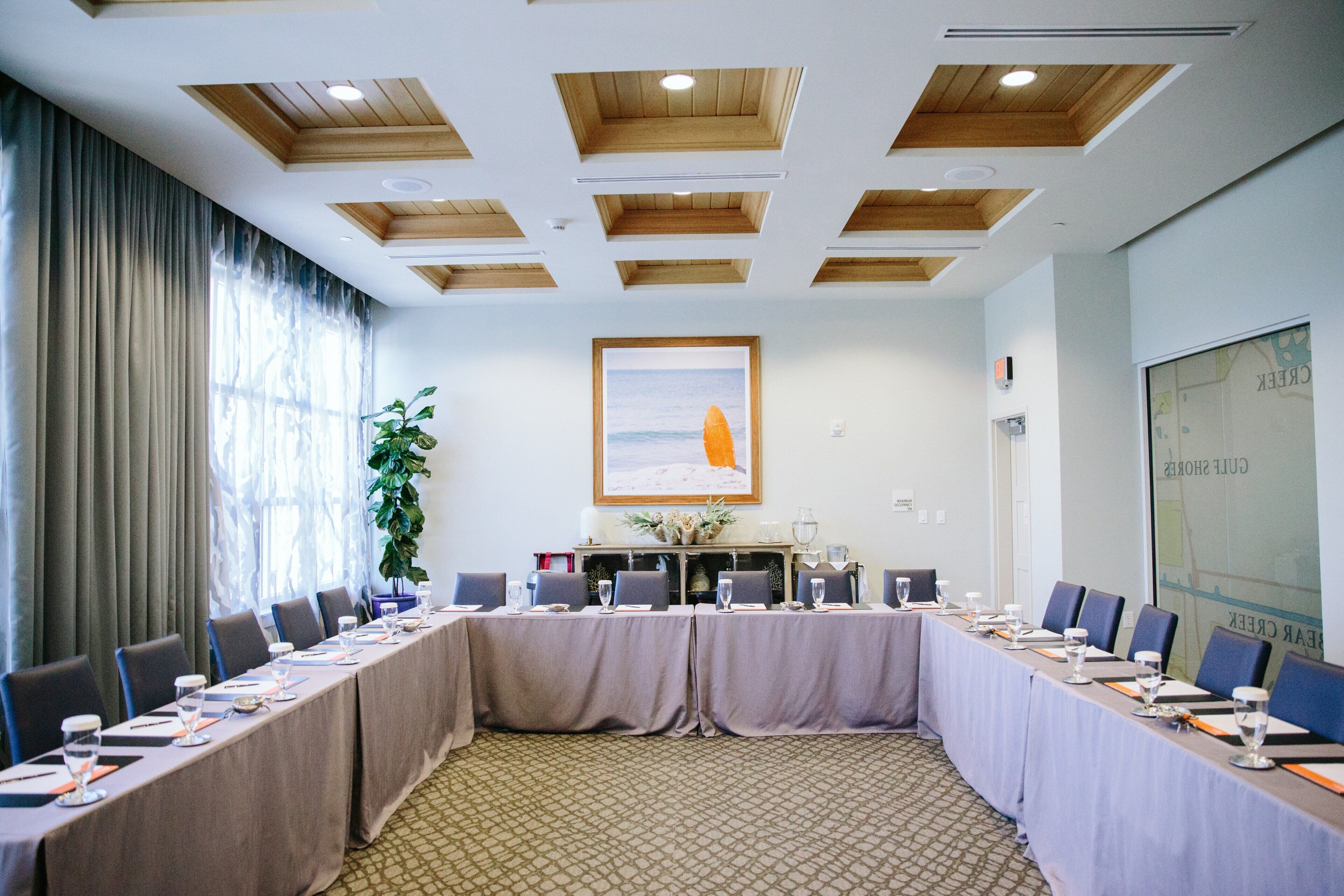 Un salón de conferencias con una larga mesa, sillas, una planta en maceta y un cuadro en la pared.