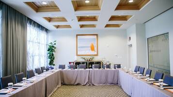 Un salón de conferencias con una larga mesa, sillas, una planta en maceta y un cuadro en la pared.
