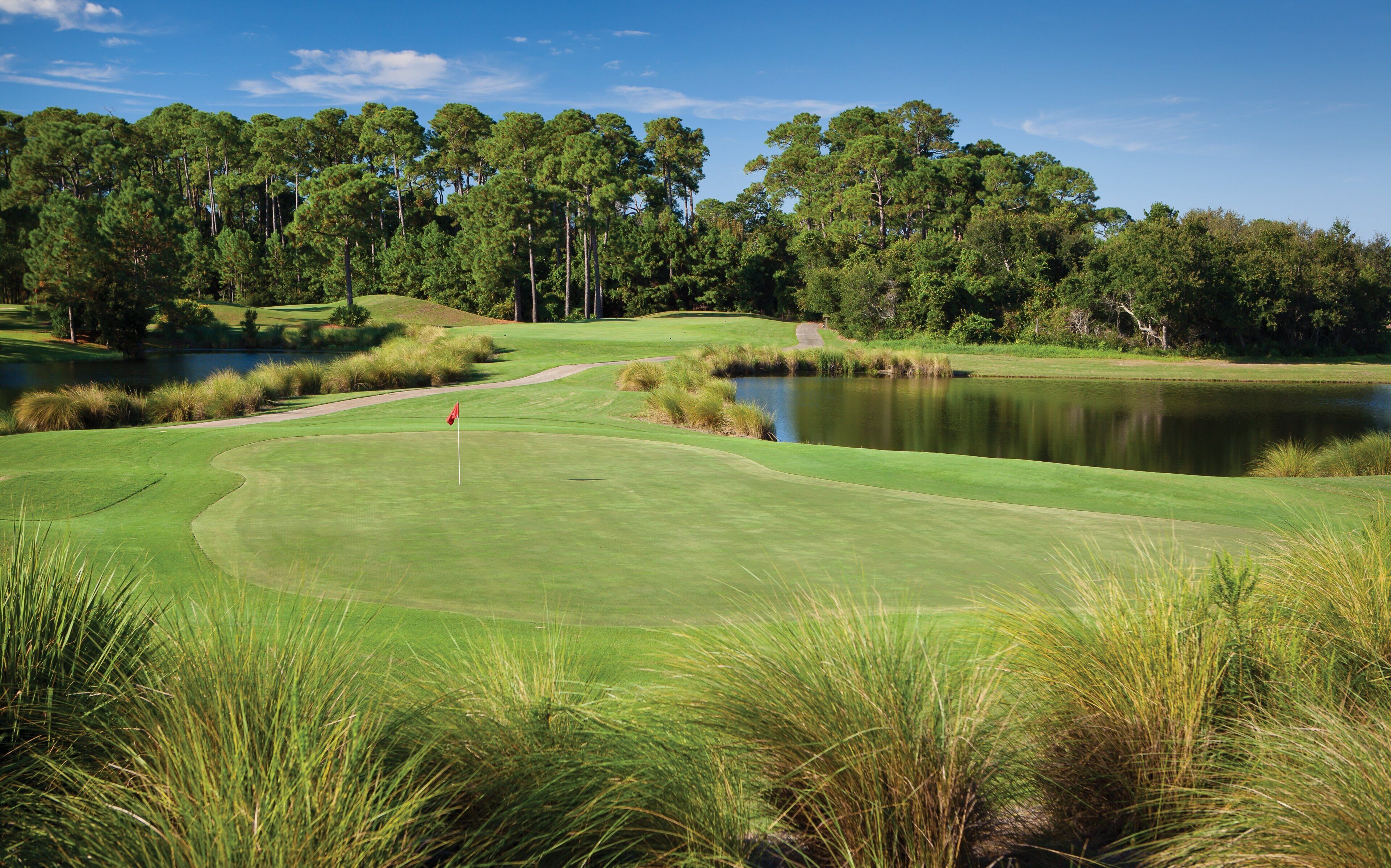 A golf course with a pond, trees, and a flag on the green.