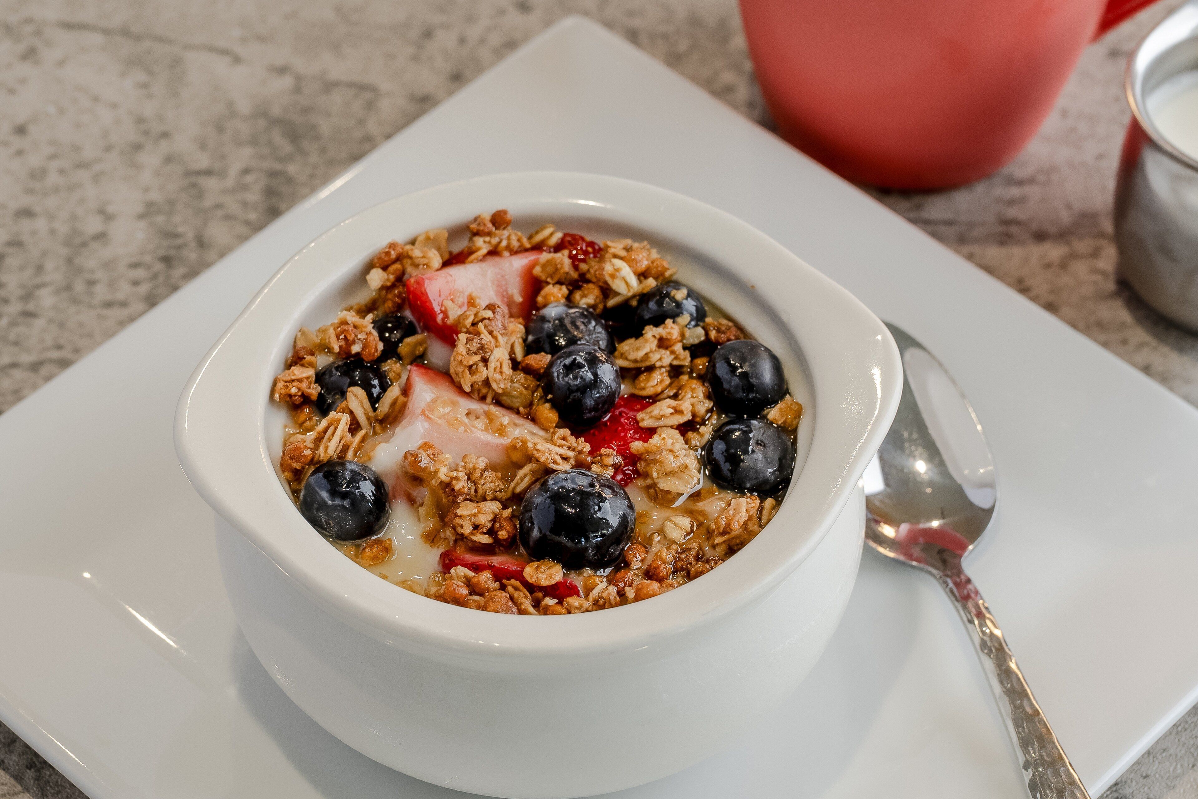 A bowl of cereal with strawberries and blueberries on a white plate.