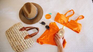 A bed with a white textured bedspread, a straw bag, a straw hat, sunglasses, and an orange bikini set.
