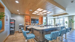 A modern bar area with a central island, bar stools, and a variety of bottles and glasses on shelves.