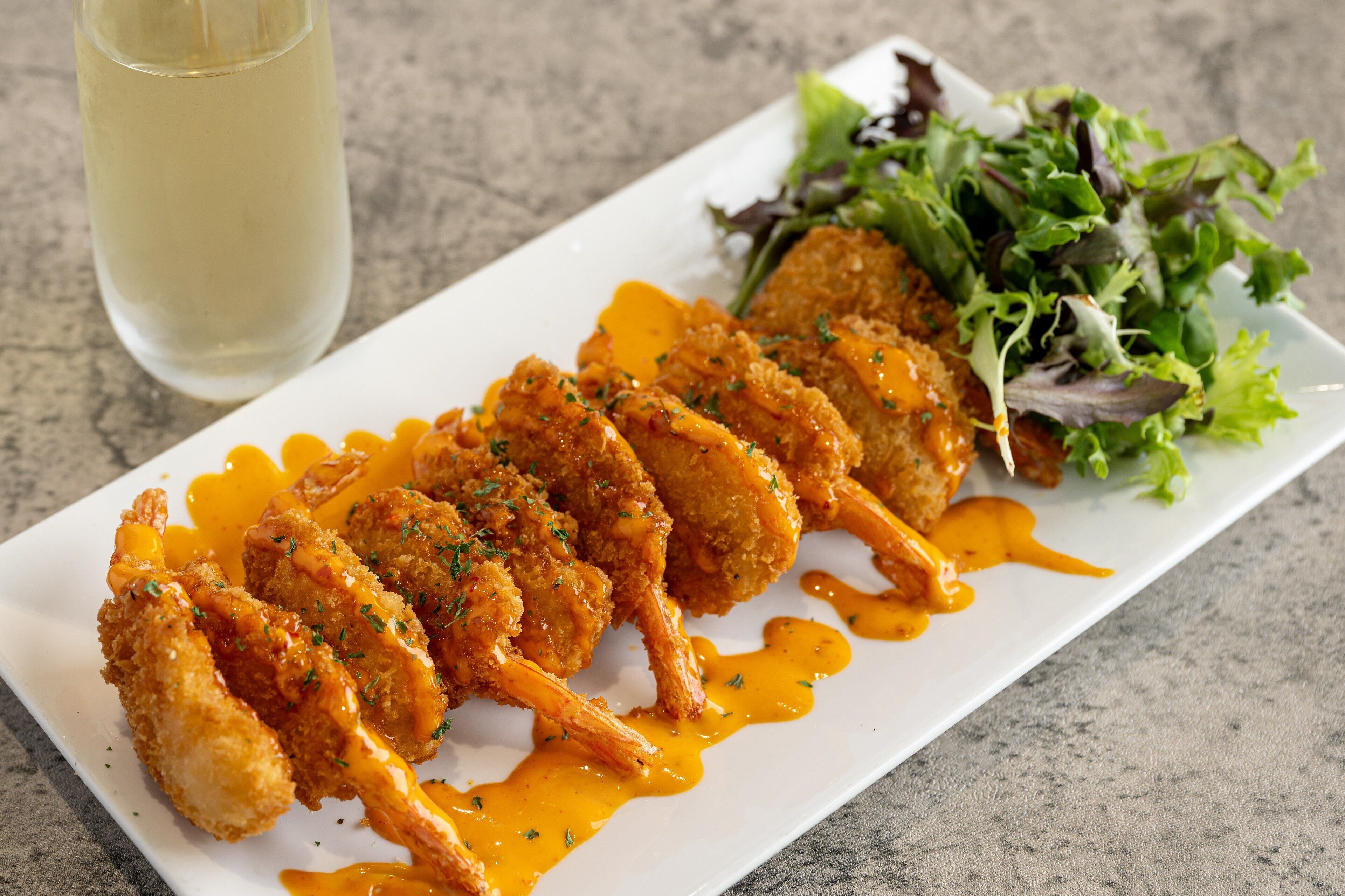 A plate of breaded and fried chicken wings with a side of mixed greens and a glass of white wine.