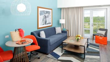 A modern hotel room with a blue sofa, orange chairs, a small table with a lamp, a large window with curtains, and a balcony with a view.