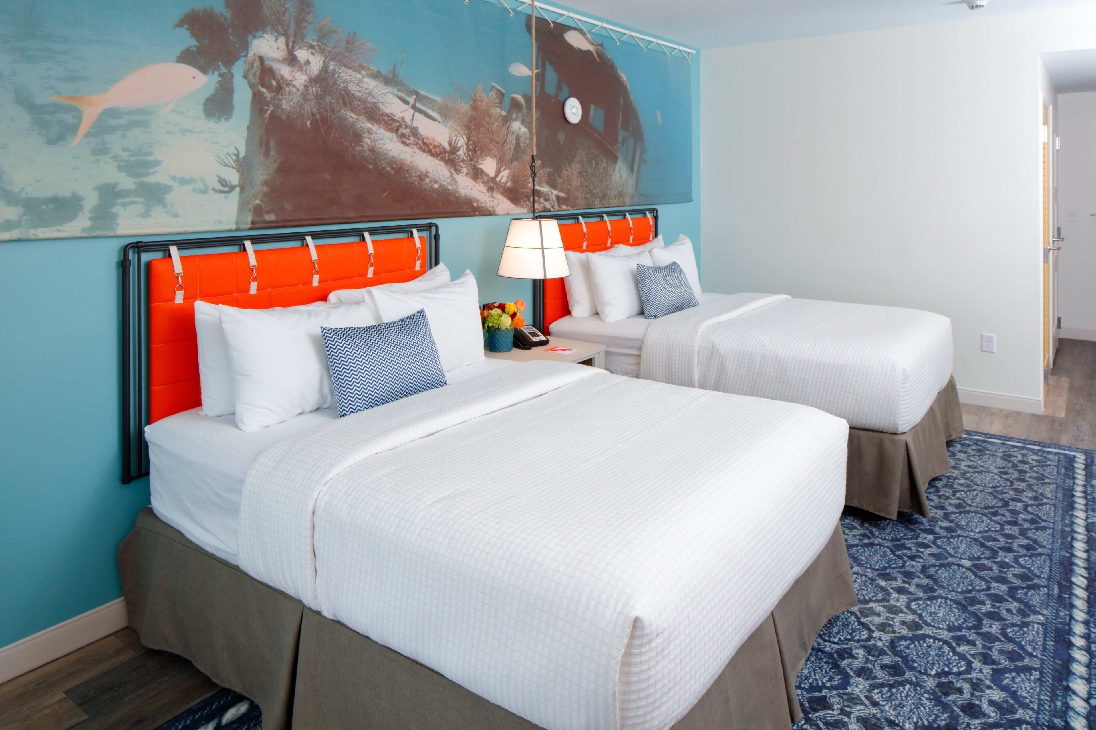 Ein Hotelzimmer mit zwei Betten, einem blau-weißen Teppich und einem großen Wandgemälde.