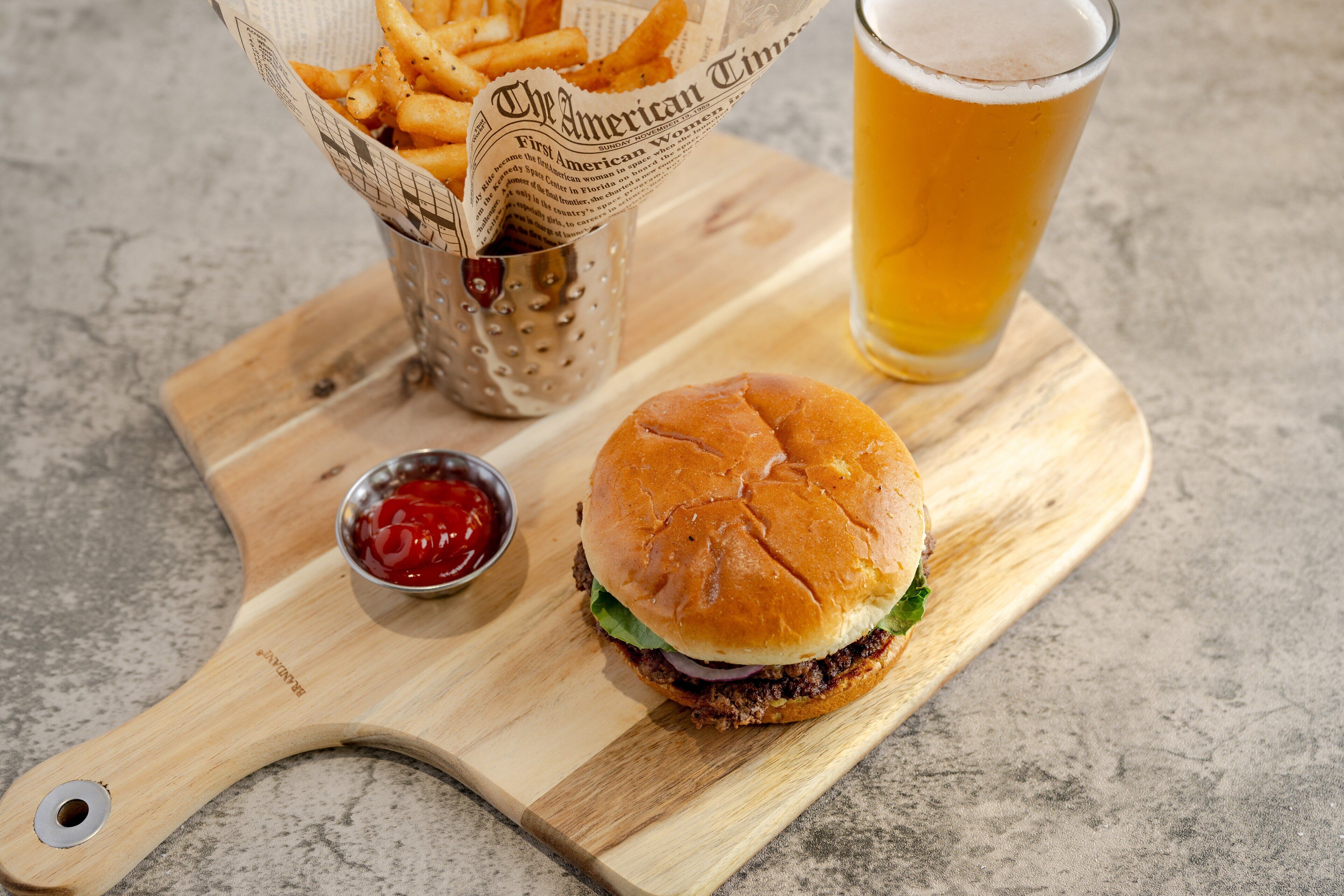 Una hamburguesa, papas fritas y una cerveza en una tabla de madera.