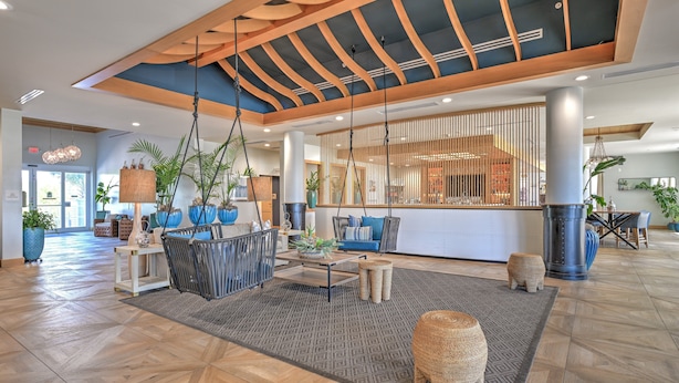 A spacious lobby with a wooden ceiling, a reception desk, seating area, and large potted plants.
