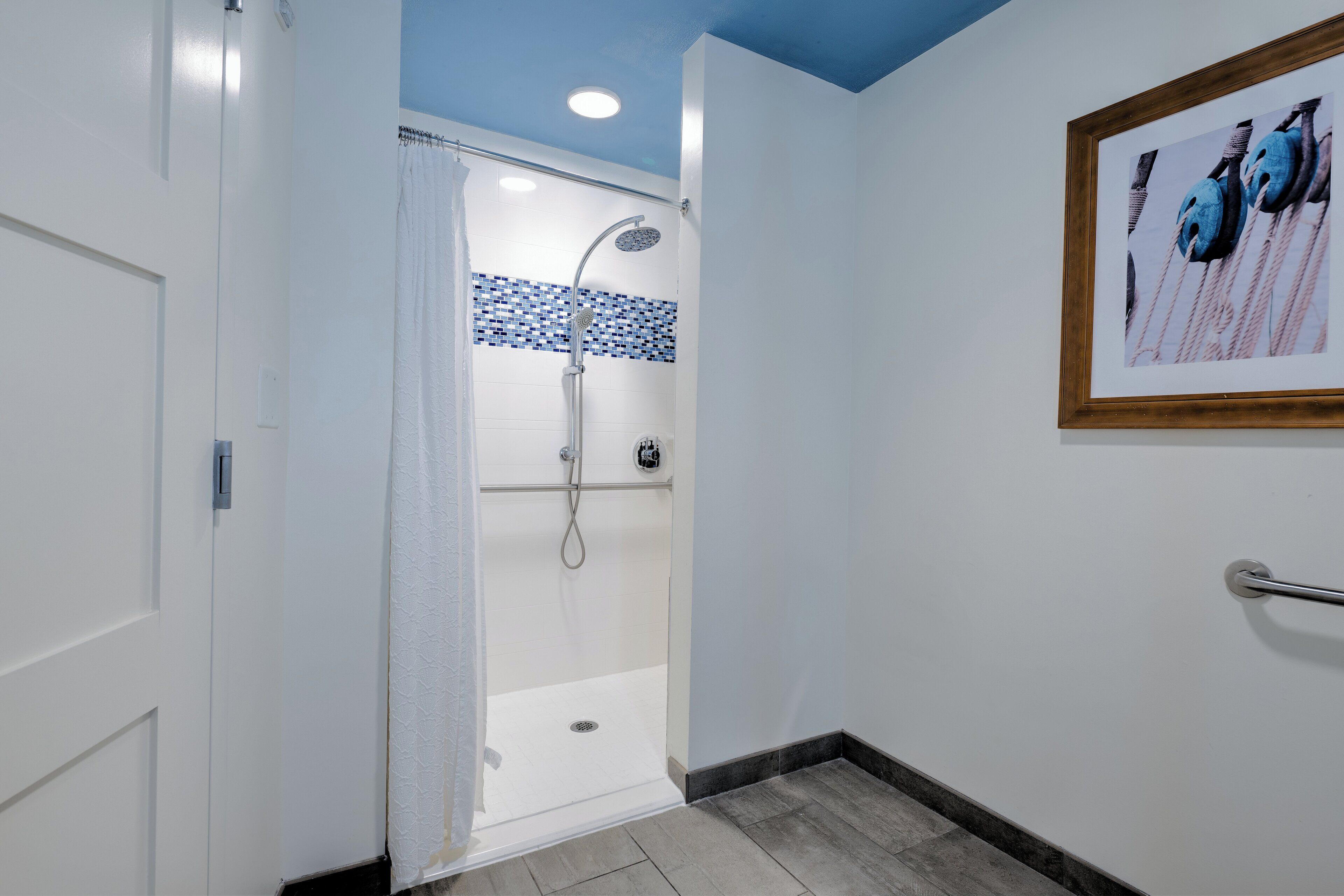 Un espace douche doté d’une porte en verre, d’un pommeau de douche carrelé et d’un tableau encadré au mur.