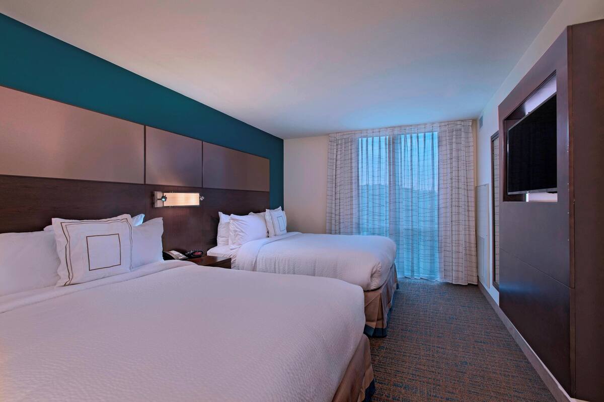 A hotel room with two beds, a large TV, and a window with curtains.