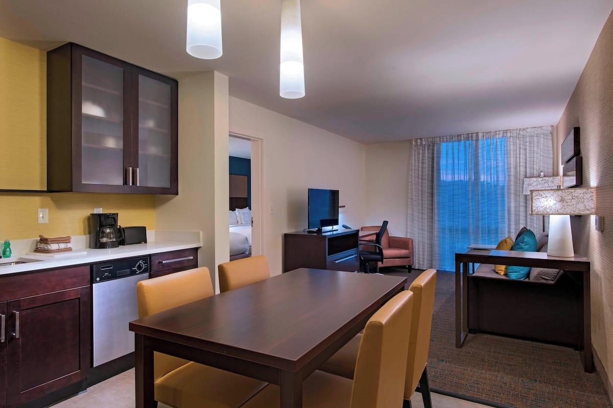 A hotel room with a dining area, kitchenette, and a bed.