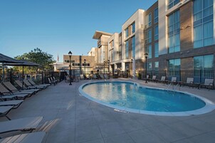 Un hotel moderno con piscina, sillas de descanso y un patio cubierto.
