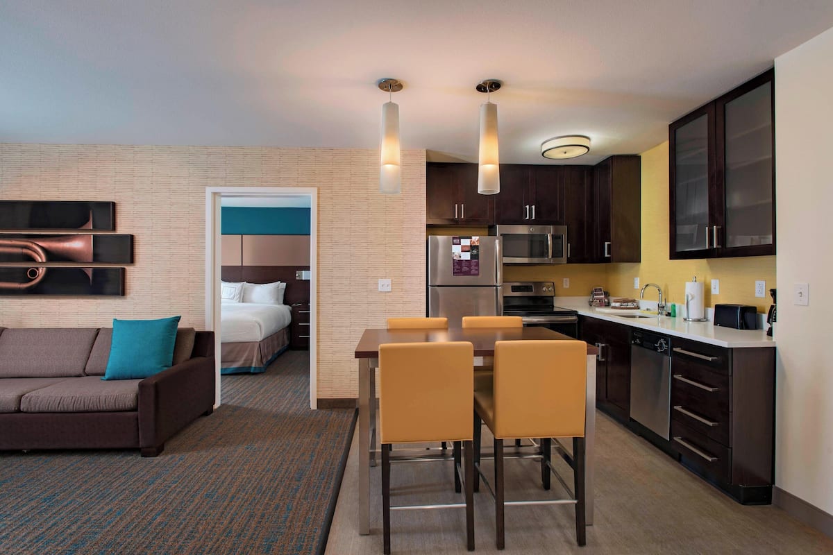 A modern hotel room with a living area, kitchenette, and a separate bedroom.