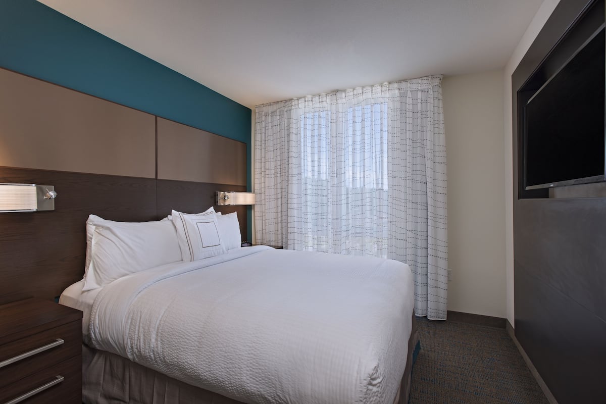 A neatly made bed with white linens, a headboard, and a bedside table with a lamp.