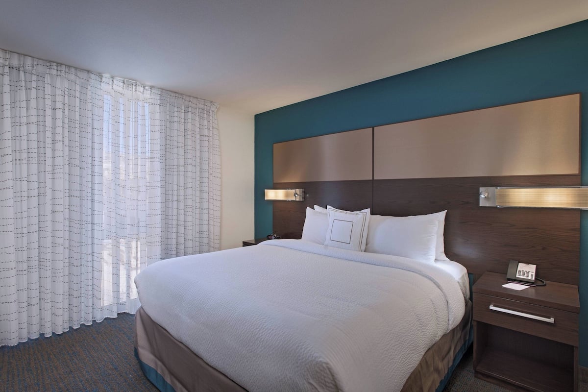 A hotel room with a large bed, a nightstand with a phone, and a headboard with a light panel.