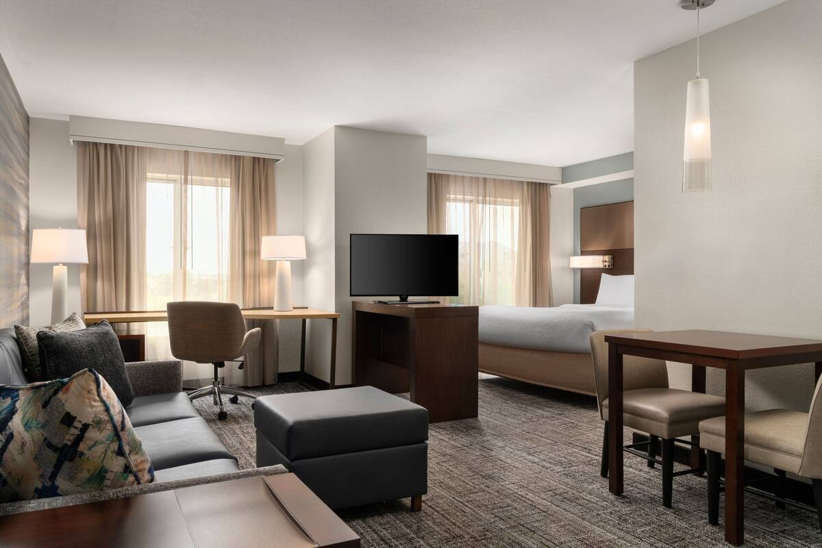 Habitación de hotel con sofá, reposapiés, televisor, escritorio y cama.