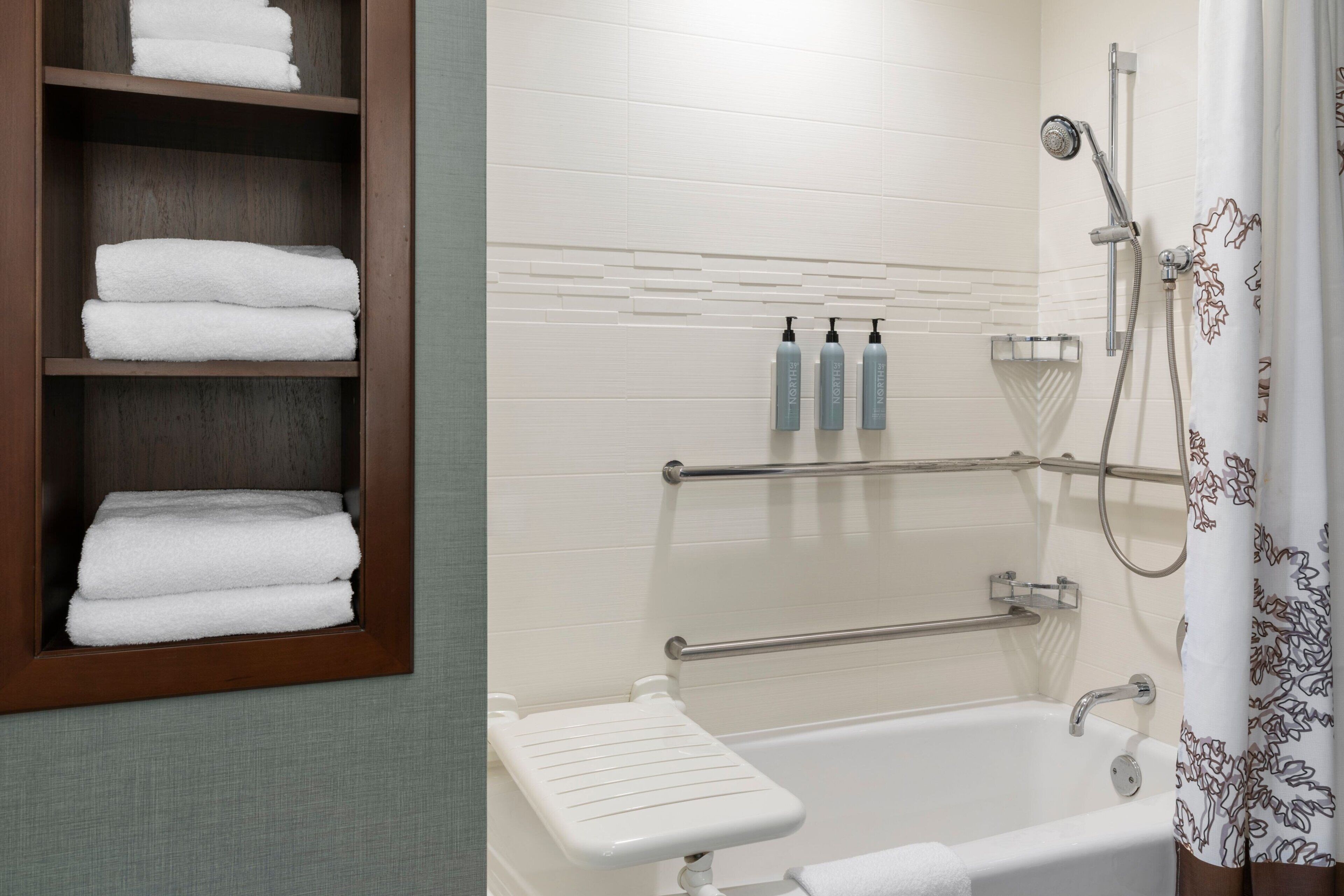 A bathroom with a bathtub, a shower, a towel rack with folded towels, and toiletries on the wall.