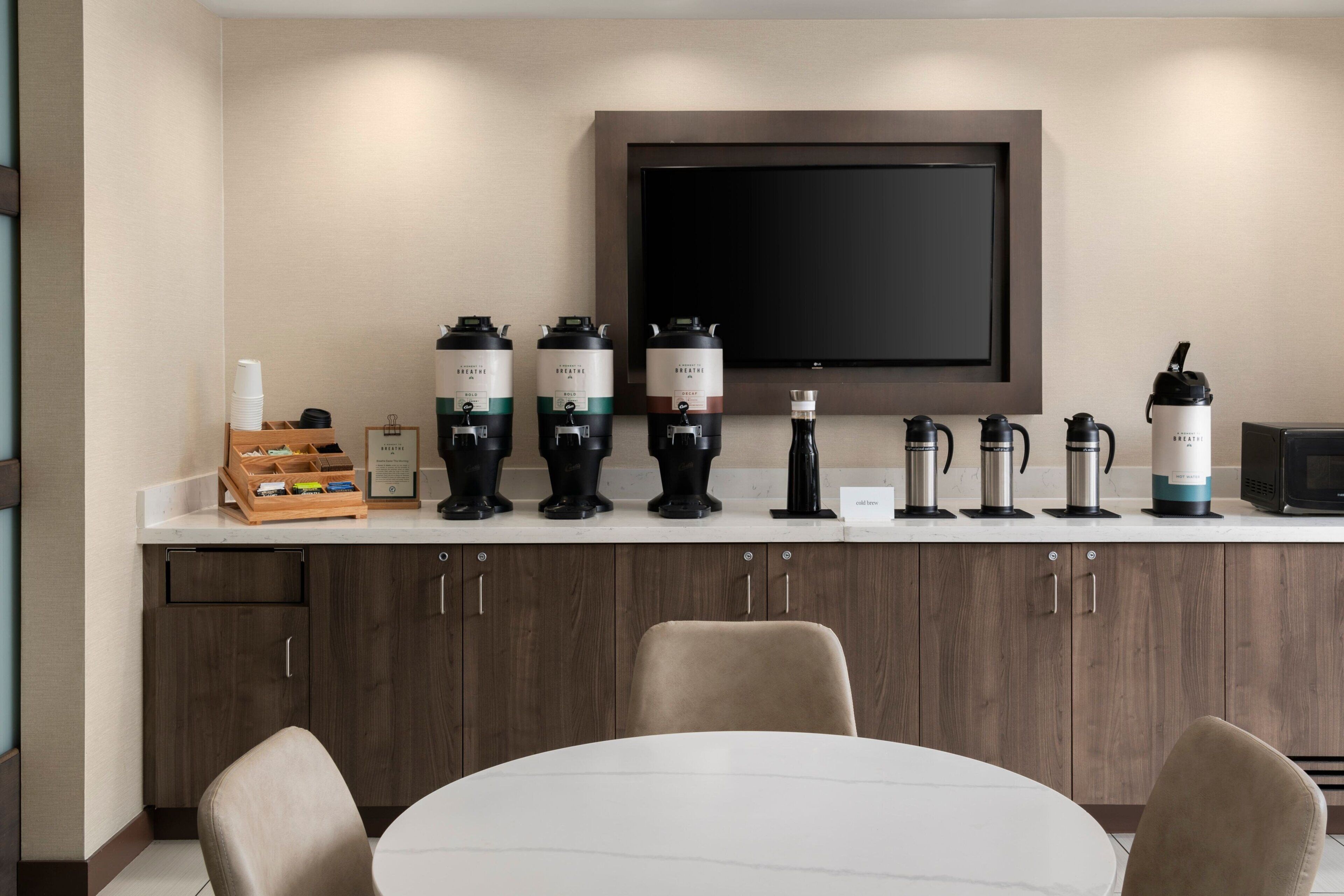 Una cocina moderna con un televisor de pantalla plana sobre la encimera, equipada con varias cafeteras y un hervidor.
