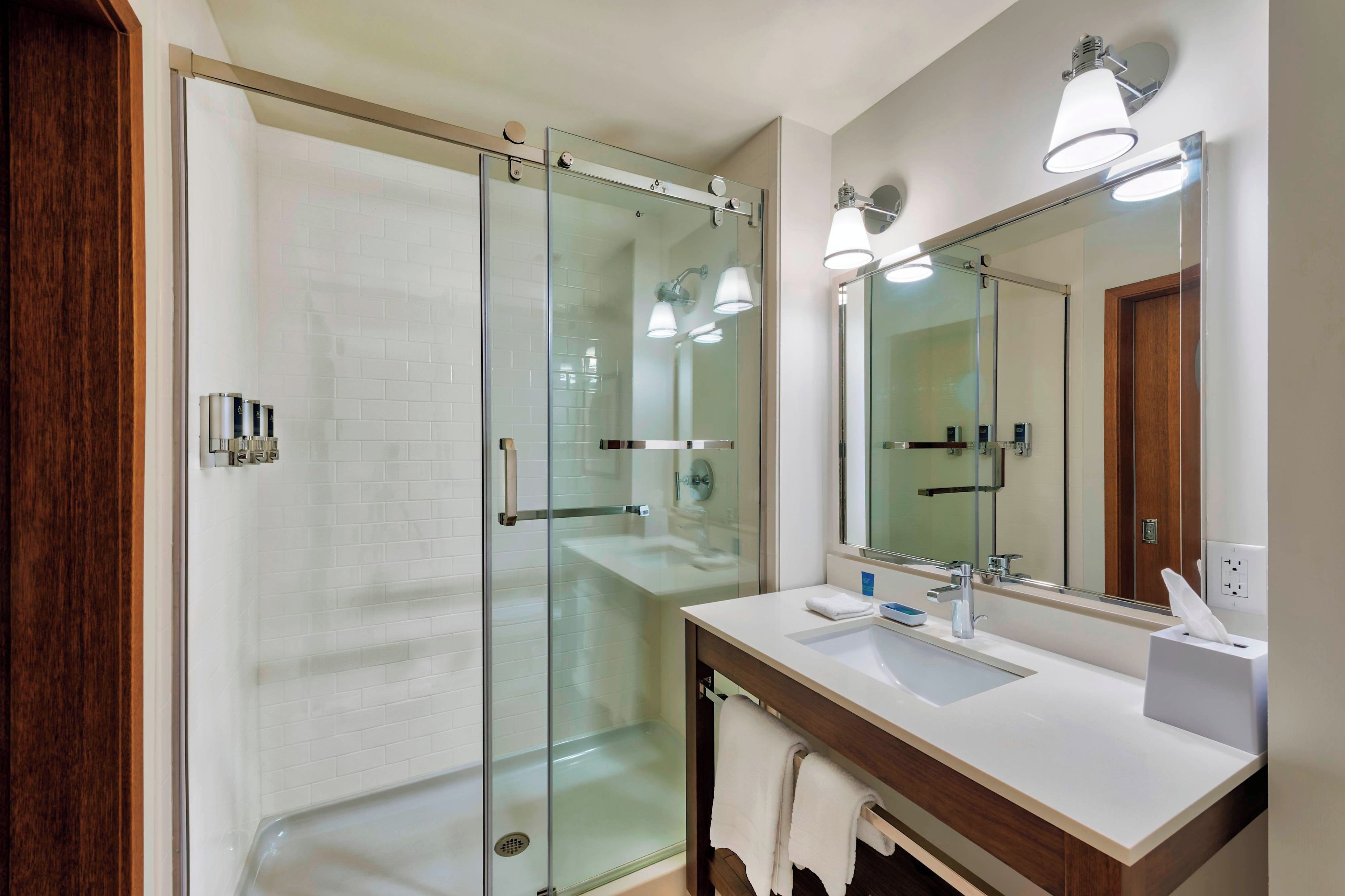 A modern bathroom with a glass shower enclosure, a large mirror, and a white sink with a towel rack.