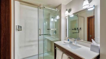 A modern bathroom with a glass shower enclosure, a large mirror, and a white sink with a towel rack.