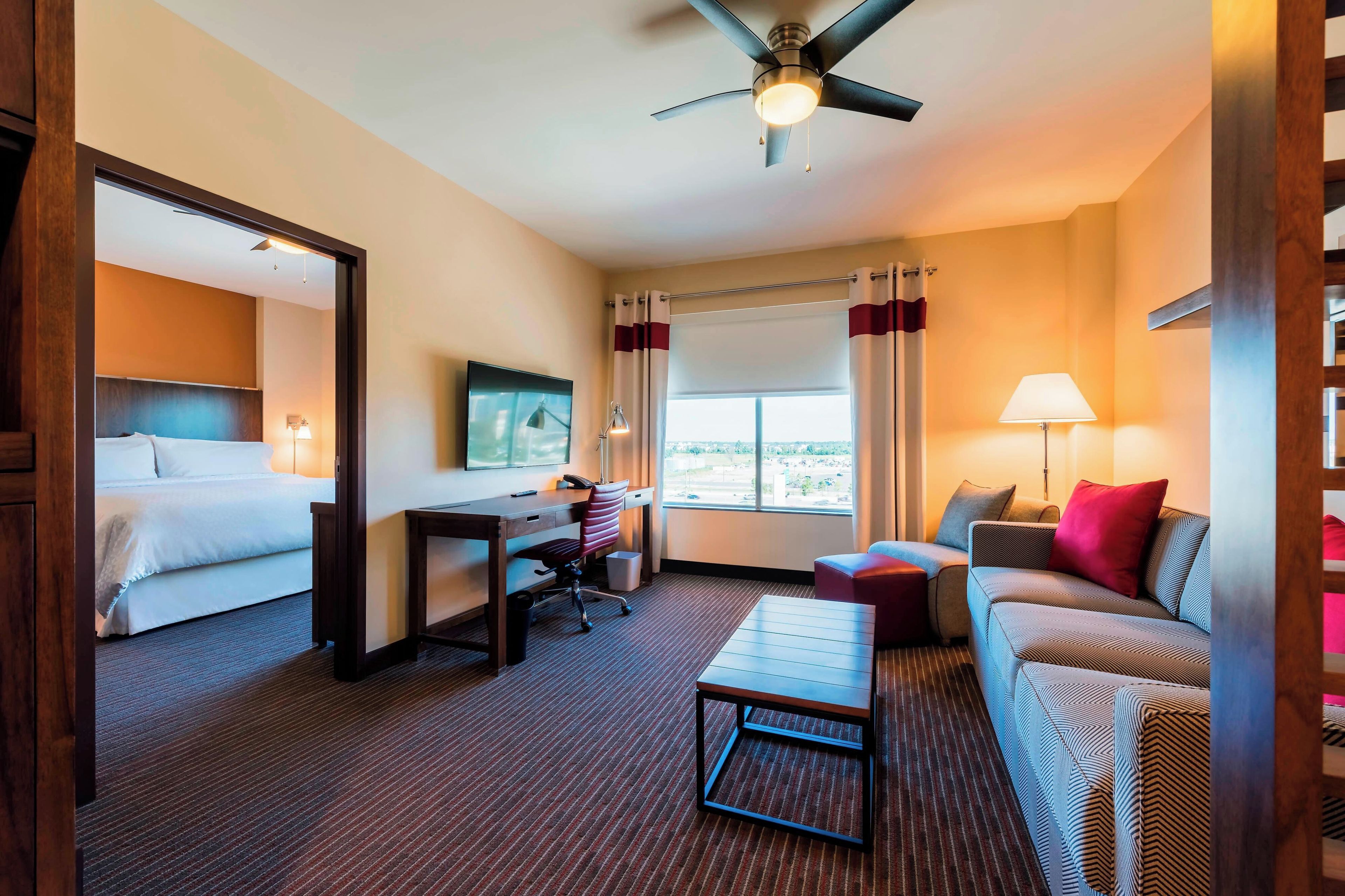 Habitación de hotel con cama, escritorio, silla, sofá y vistas a la ciudad a través del ventanal.