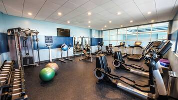A gym with treadmills, elliptical machines, free weights, and exercise balls.