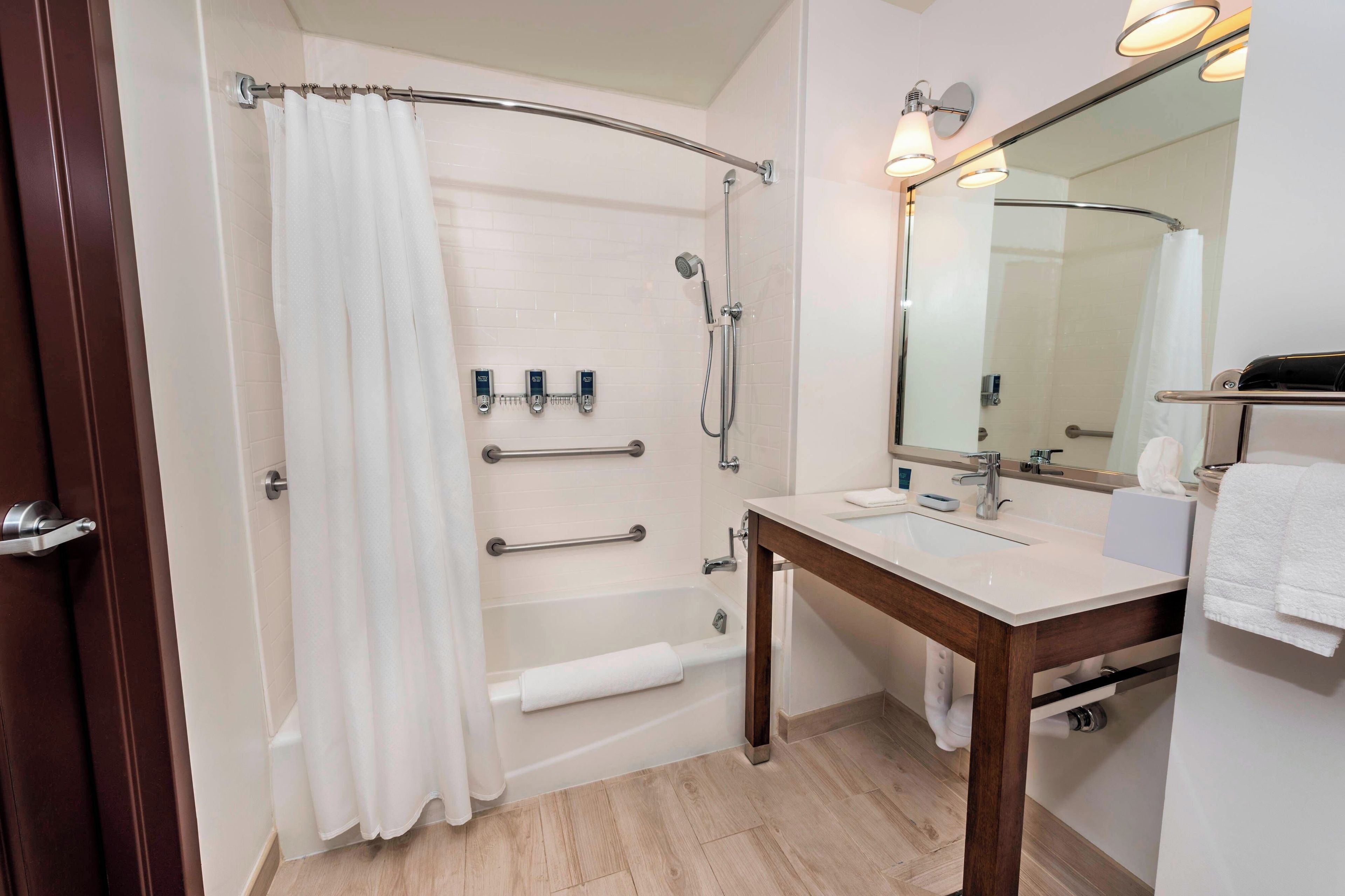 Een badkamer met douche, toilet en wastafel, voorzien van handgrepen en een handdoekrek.