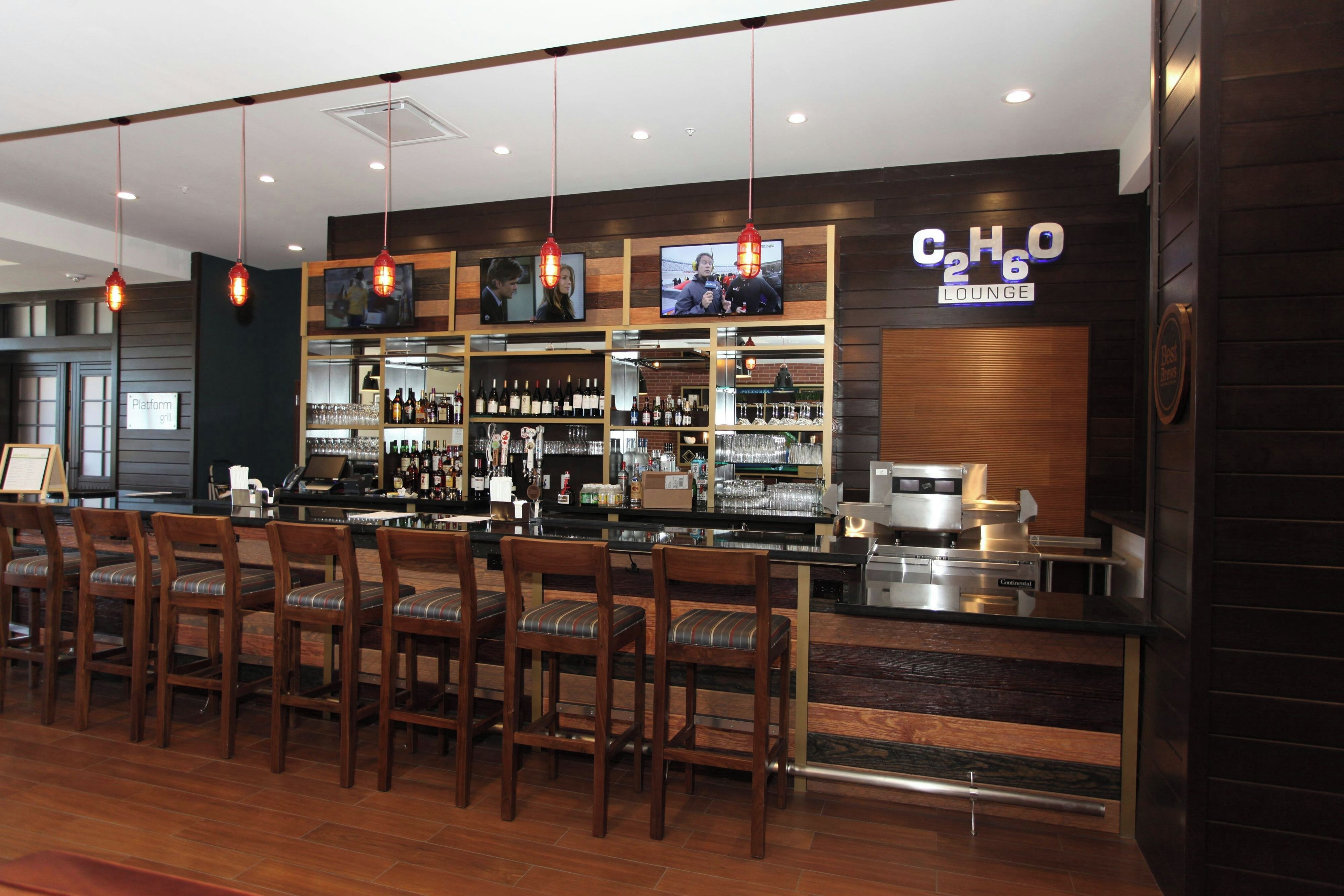 A bar area with wooden chairs, a counter with a coffee machine, and shelves stocked with bottles and glasses.