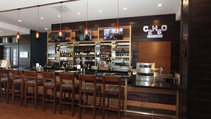 A bar area with wooden chairs, a counter with a coffee machine, and shelves with bottles.