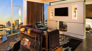A modern living room with a city view, a flat-screen TV, and a dining area with a table and chairs. - Thompson Nashville, by Hyatt (Nashville)