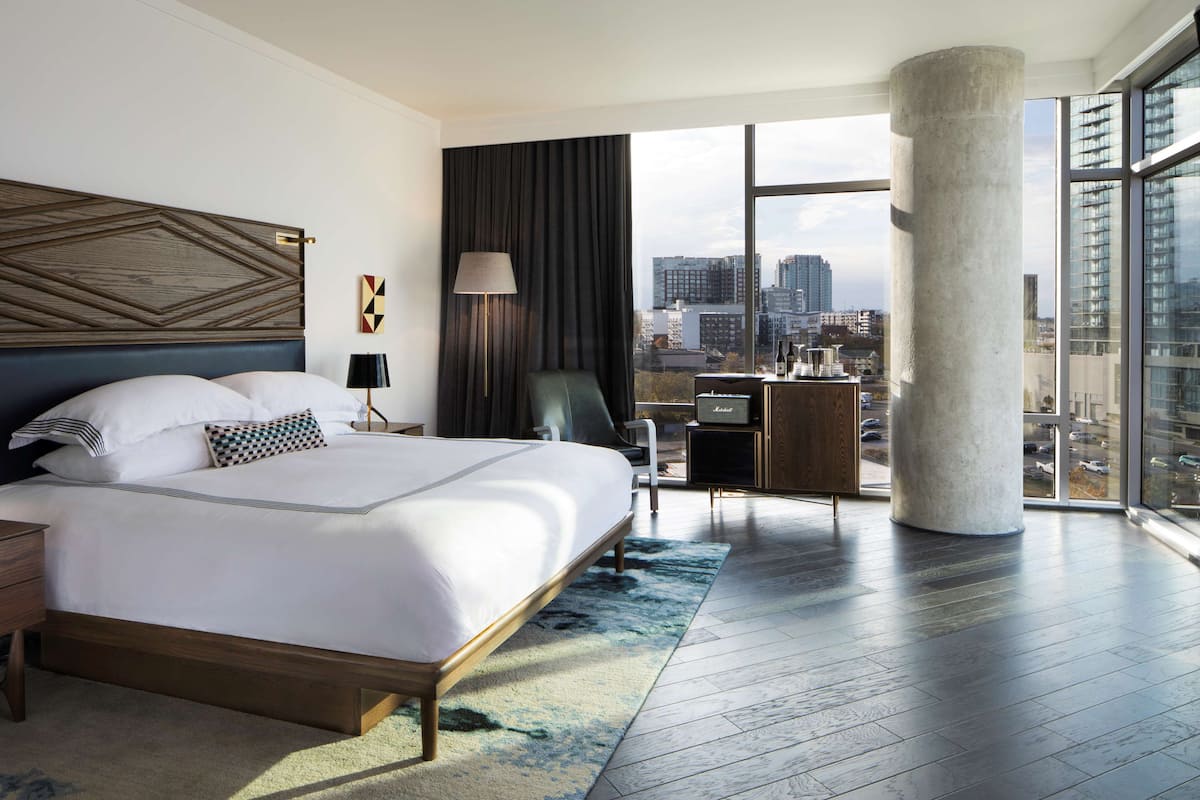 Une chambre d’hôtel moderne dotée d’un grand lit, d’un bureau, d’une chaise et offrant une vue sur la ville grâce à de grandes fenêtres.