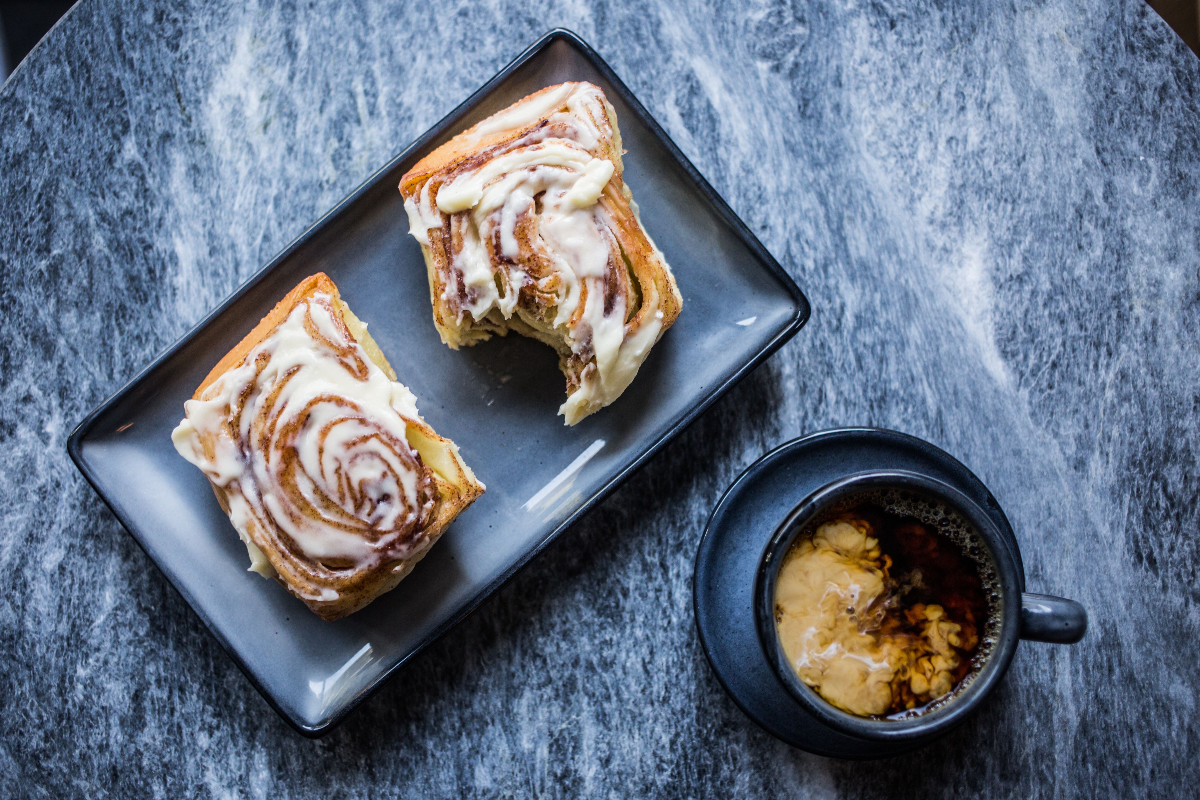 Two pastries on a dark plate with a cup of coffee beside it.