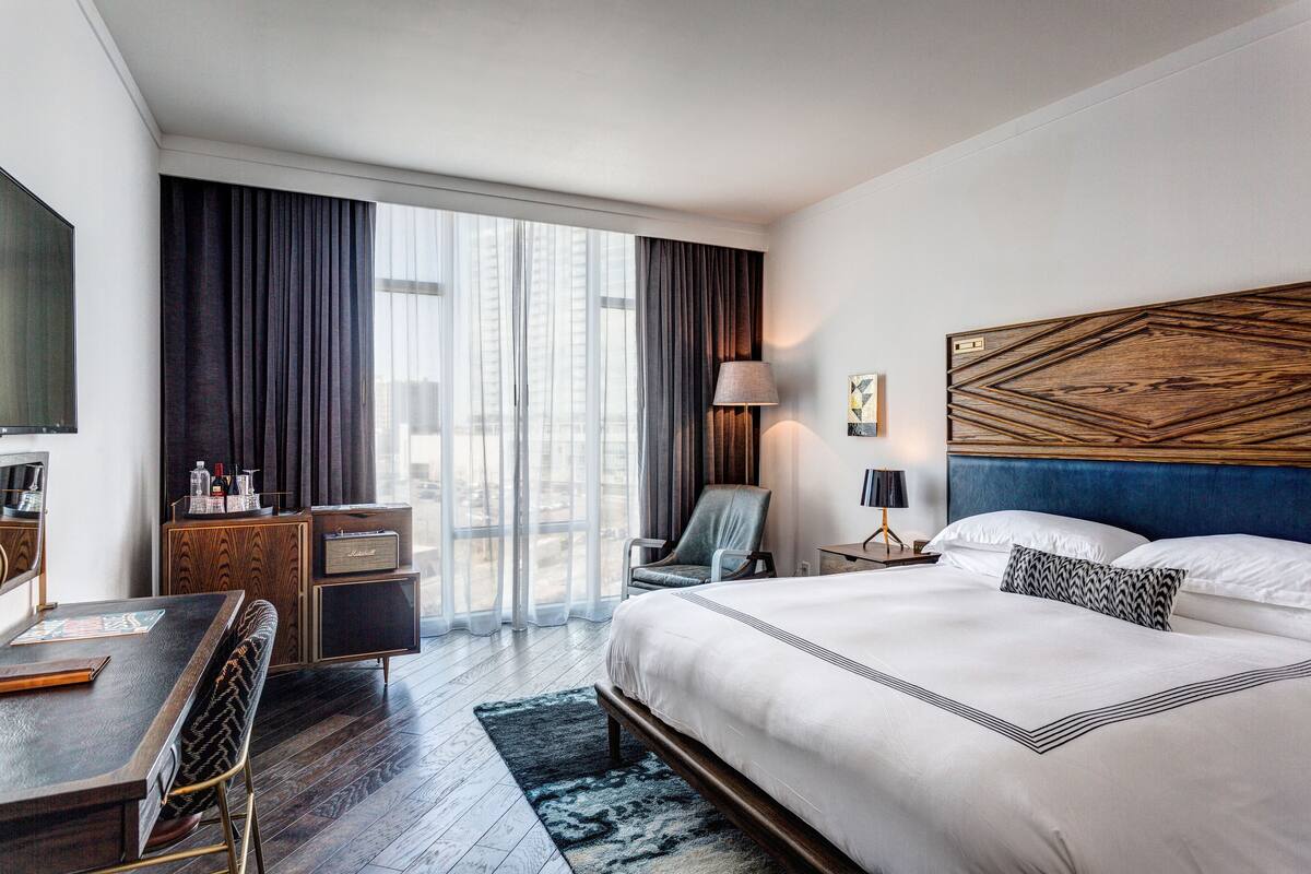 Une chambre d’hôtel moderne dotée d’un grand lit, d’un bureau avec une chaise, d’une télévision et offrant une vue sur la ville grâce à de grandes fenêtres.