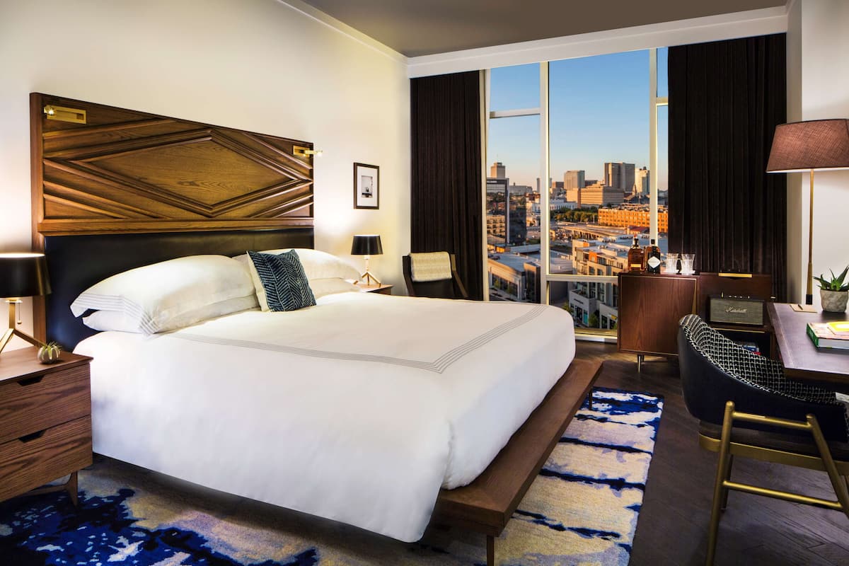 Une chambre d’hôtel avec un grand lit, un bureau, une chaise, une vue sur la ville et un panorama urbain visible par la fenêtre.