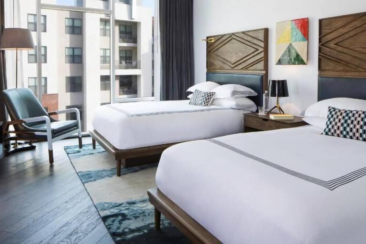 Une chambre d’hôtel avec deux lits, une chaise, une table de chevet, une lampe et une vue sur la ville.