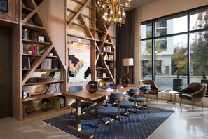 A modern library with bookshelves, a large wooden table, and comfortable seating.