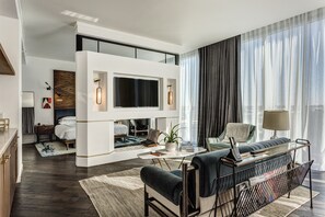 A modern living room with a flat-screen TV, a sofa, a coffee table, and a dining area with a glass top.
