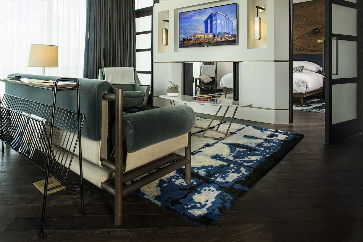 Une chambre d’hôtel moderne, équipée d’un canapé, d’une petite table, d’un téléviseur fixé au mur et d’un lit avec une tête de lit.