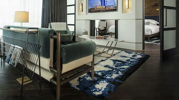 A modern hotel room with a sofa, a small table, a TV mounted on the wall, and a bed with a headboard.