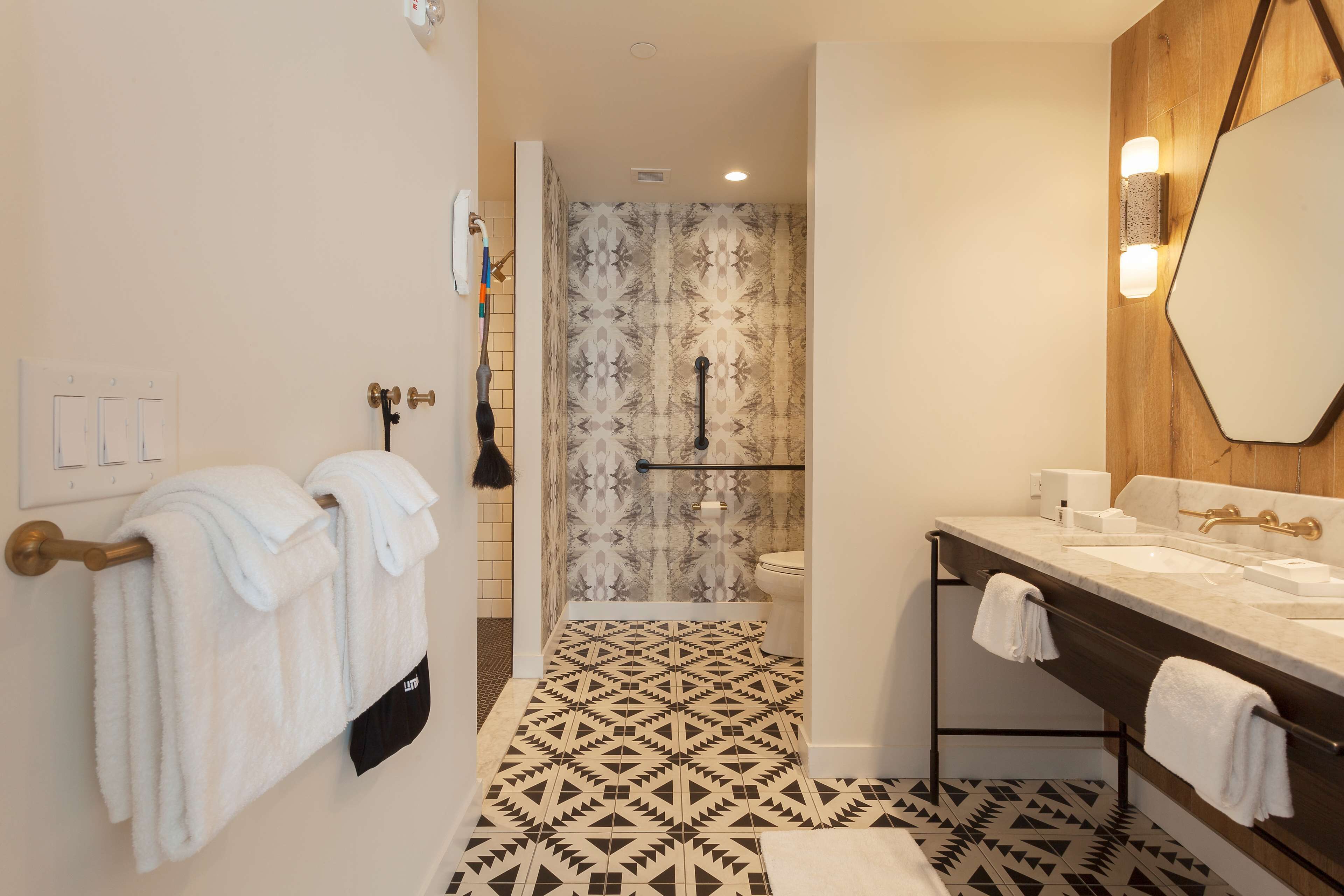 A modern bathroom with a geometric patterned floor, a large mirror, and a dual sink vanity.