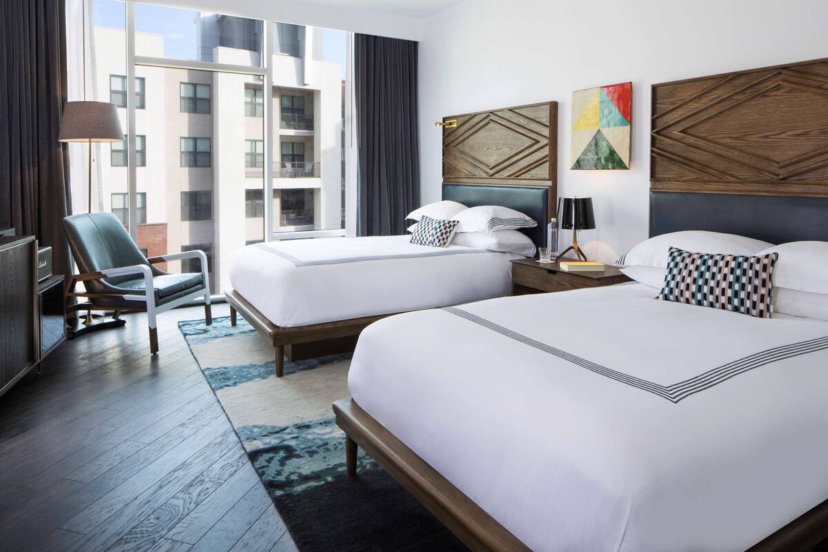 Une chambre d’hôtel avec deux lits, un bureau, une chaise et une grande fenêtre donnant sur la ville.