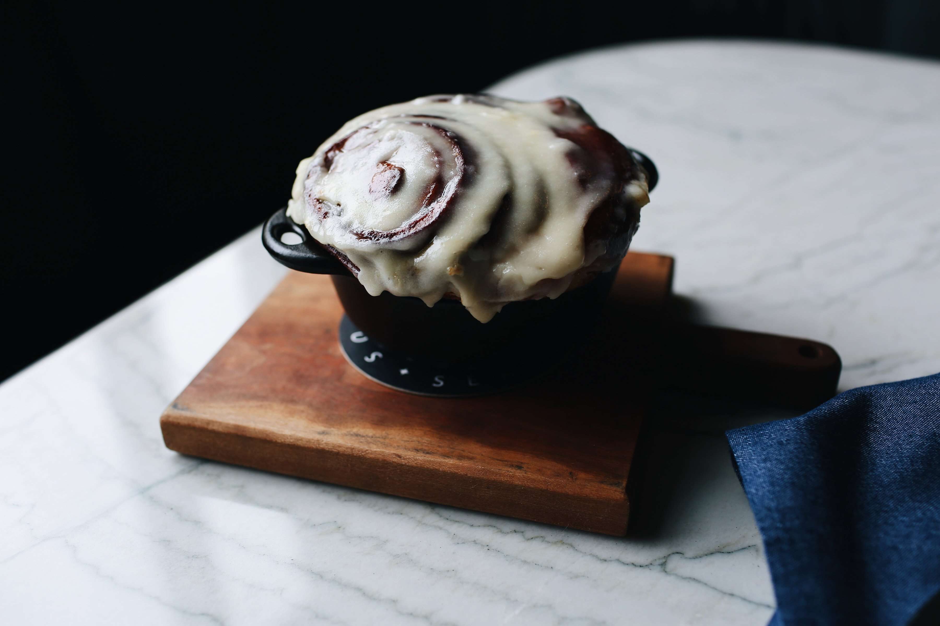 A cinnamon roll in a black mug on a wooden coaster.