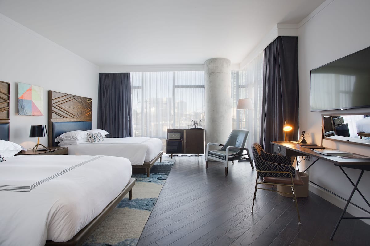Une chambre d’hôtel avec deux lits, un bureau, une chaise, une télévision et une grande fenêtre avec des rideaux.