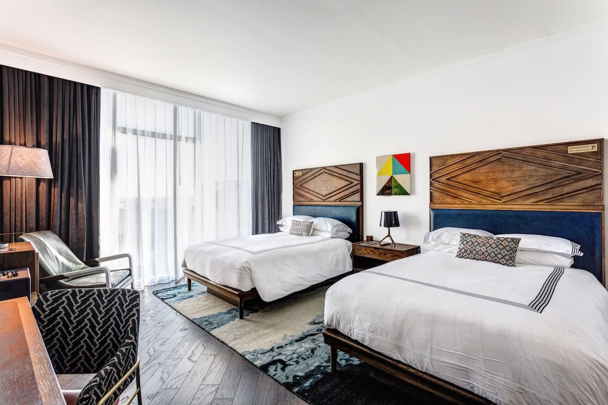 Une chambre d’hôtel avec deux lits, un bureau, une chaise, une lampe et une vue sur l’extérieur.