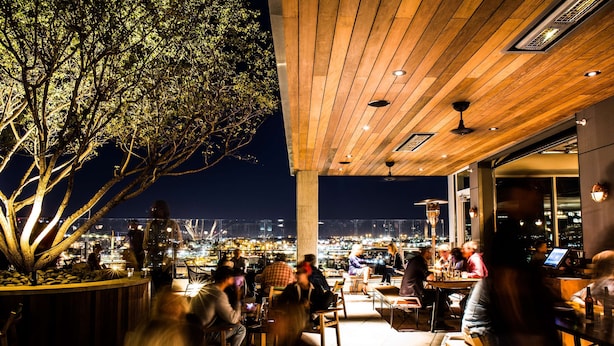 An outdoor seating area with tables and chairs, a large tree, and a view of the cityscape at night. - Thompson Nashville, by Hyatt (Nashville)