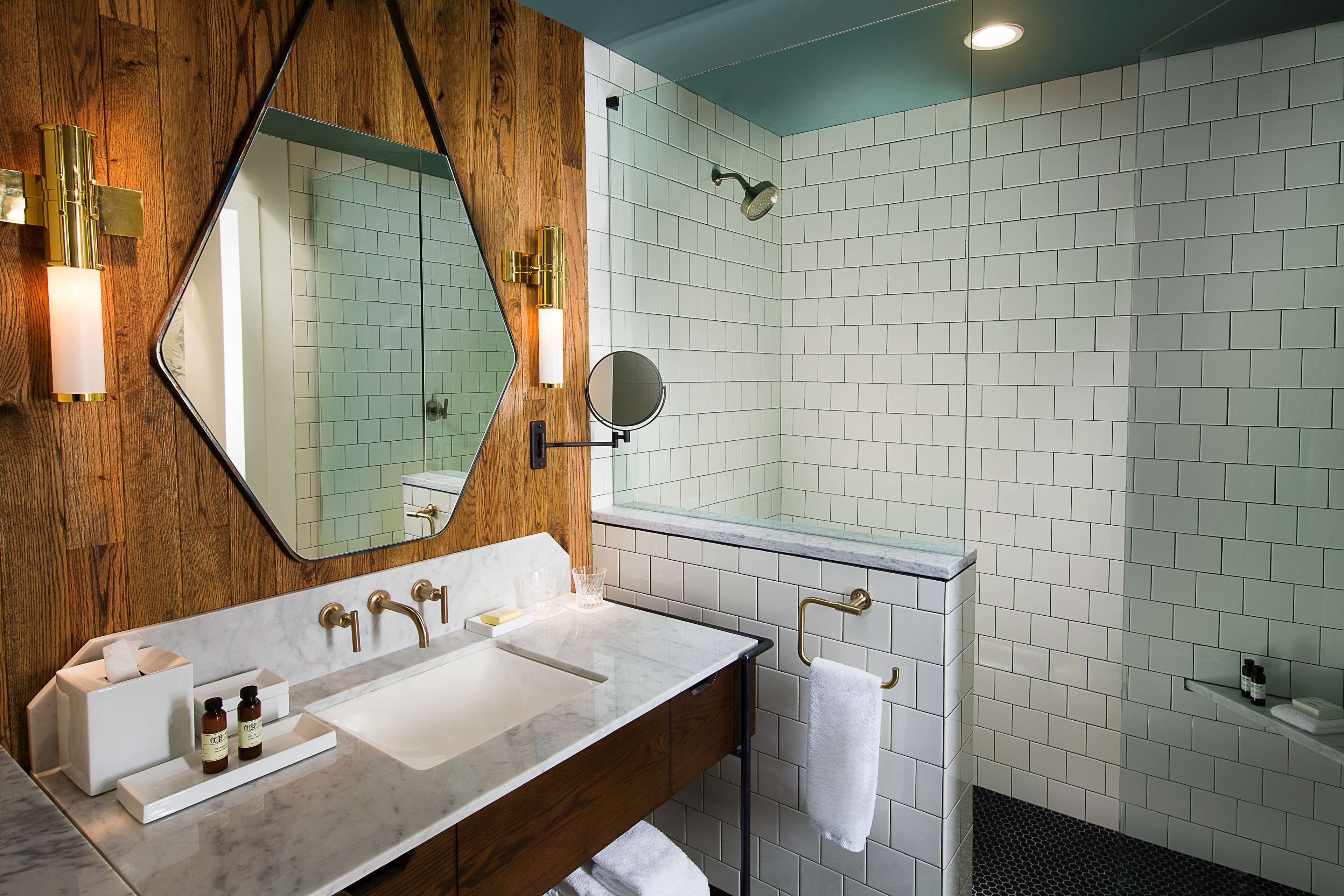 Ein modernes Badezimmer mit einem Holzausleger, einem großen Spiegel, einer Glasdusche und weiß gefliesten Wänden.