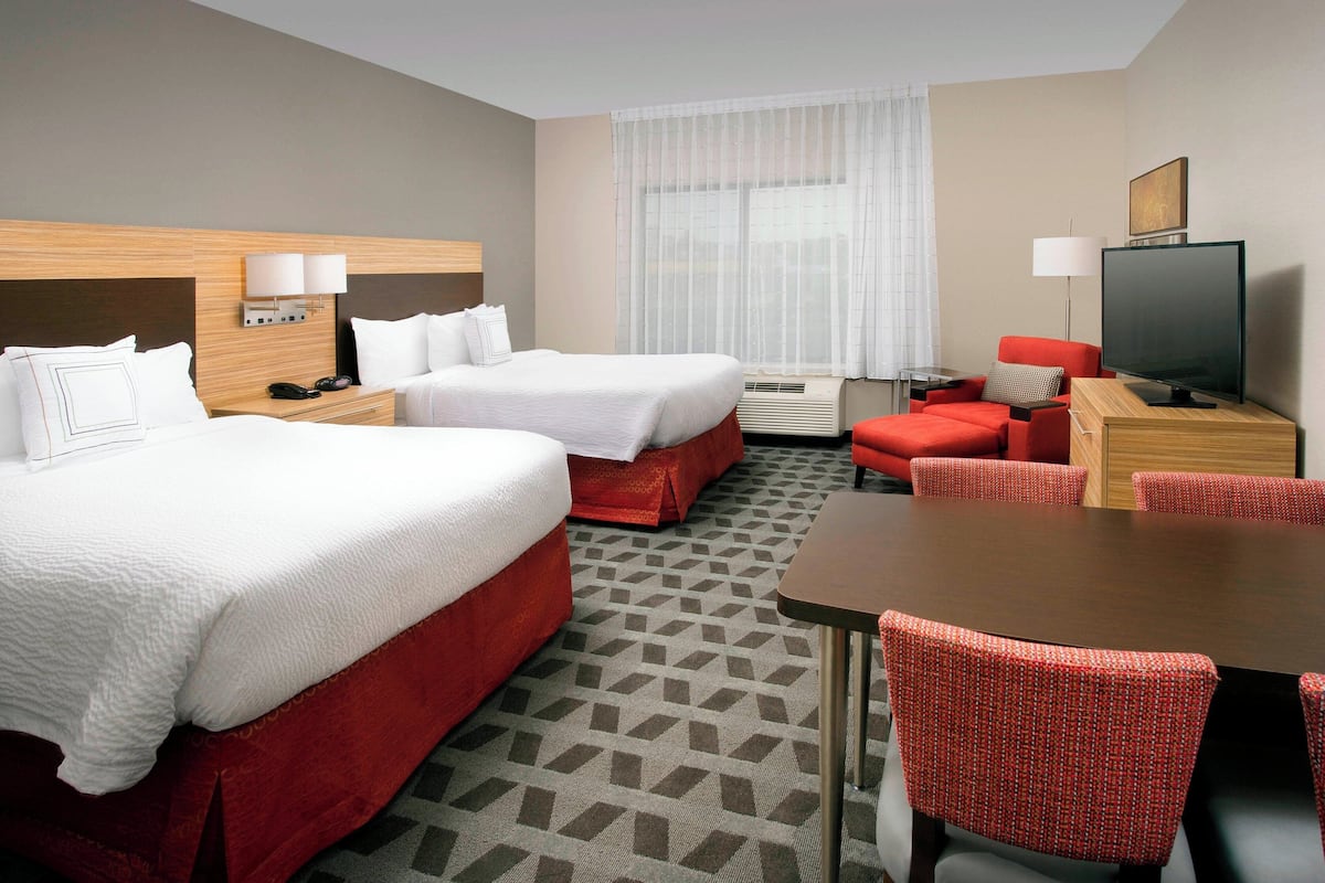 Ein Hotelzimmer mit zwei Betten, einem Esstisch, einem Fernseher und einem roten Sessel.