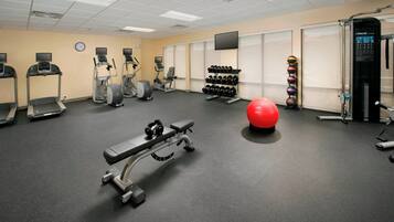 Une salle de sport équipée de tapis de course, de vélos elliptiques, d’un banc de développé couché, d’haltères et d’un ballon d’exercice rouge.